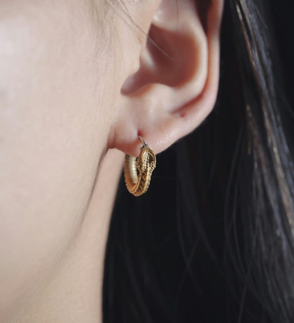 Elegant gold serpent hoop earring on woman's ear in a fashion portrait.